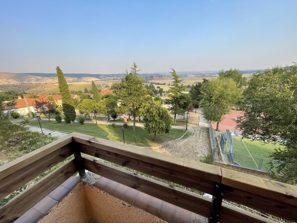 Vista desde un balcón sobre un parque con árboles, una pista de atletismo y colinas a lo lejos.