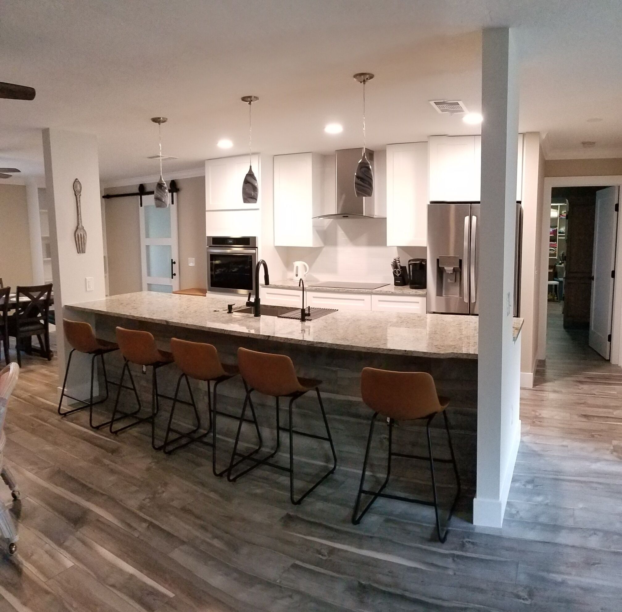 A modern kitchen with a central island, bar stools, stainless steel appliances, and pendant lighting.