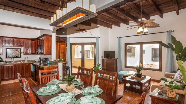 A spacious kitchen with wooden cabinets, a dining area with a large wooden table set for six, and a ceiling fan. - Gecko Getaway- a stone's throw from West Bay Beach (Roatan)