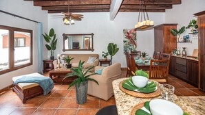 A spacious living area with a sofa, coffee table, and dining table set for a meal. There are potted plants and a ceiling fan. - Gecko Getaway- a stone's throw from West Bay Beach (Roatan)