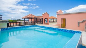 A swimming pool with a tiled edge, a gazebo, and a building with a pink facade. - Gecko Getaway- a stone's throw from West Bay Beach (Roatan)