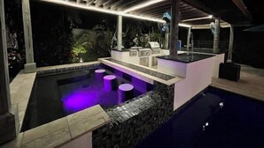 A modern outdoor pool area with a built-in bar, seating, and a pergola overhead. - The WaterSun Oasis - Luxury Private Pool & Spa (Naples)