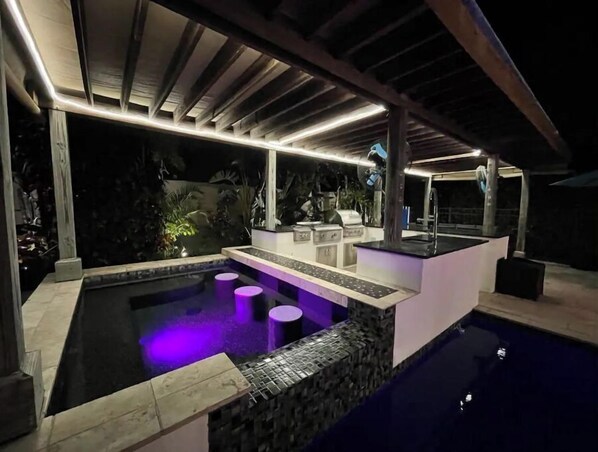 A modern outdoor pool area with a built-in bar, seating, and a pergola overhead.
