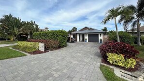 A residential driveway leading to a house with a garage, surrounded by landscaped gardens and palm trees. - The WaterSun Oasis - Luxury Private Pool & Spa (Naples)