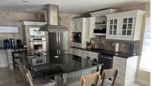 A modern kitchen with a large island, stainless steel appliances, and white cabinetry. - The WaterSun Oasis - Luxury Private Pool & Spa (Naples)