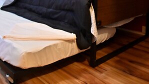 Een eenpersoonsbed met een zwart frame en een matras met een wit laken en een beige deken. De muur achter het bed is rood met een baksteenmotief.