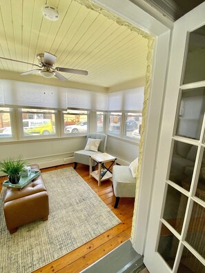 A cozy room with a ceiling fan, a bay window with blinds, a brown leather ottoman, a small table, and a chair. - Everything you need! Steps to Beach-Margate-Restaurants-Stores -Sleeps 4 guests (Ventnor City)