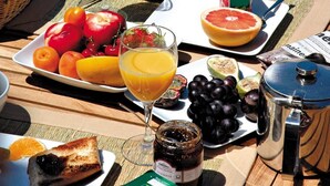 A breakfast setup by a pool with fruits, juice, bread, and a grill.
