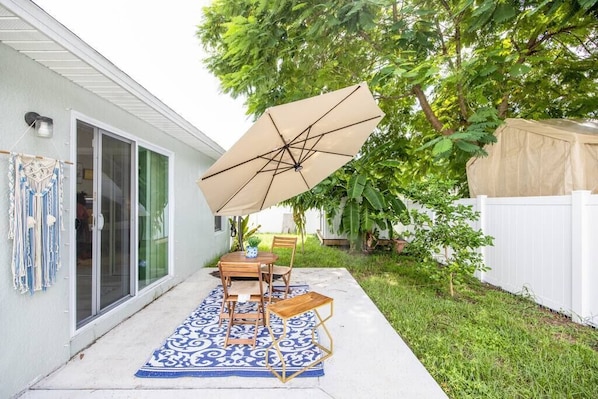 Relax on the patio with a dining table and comfortable seating for four, shaded by a large umbrella.