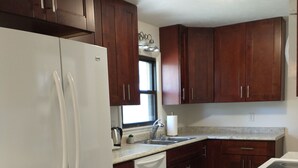 Una cocina con armarios de madera, un refrigerador blanco, un lavamanos y un ventanal.