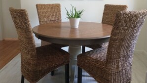 Una mesa de comedor redonda con cuatro sillas tejidas, una planta en maceta y una lámpara de araña.