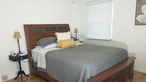 Una cama bien tendida con una colcha gris y una almohada amarilla, flanqueada por dos mesitas de noche con lámparas.