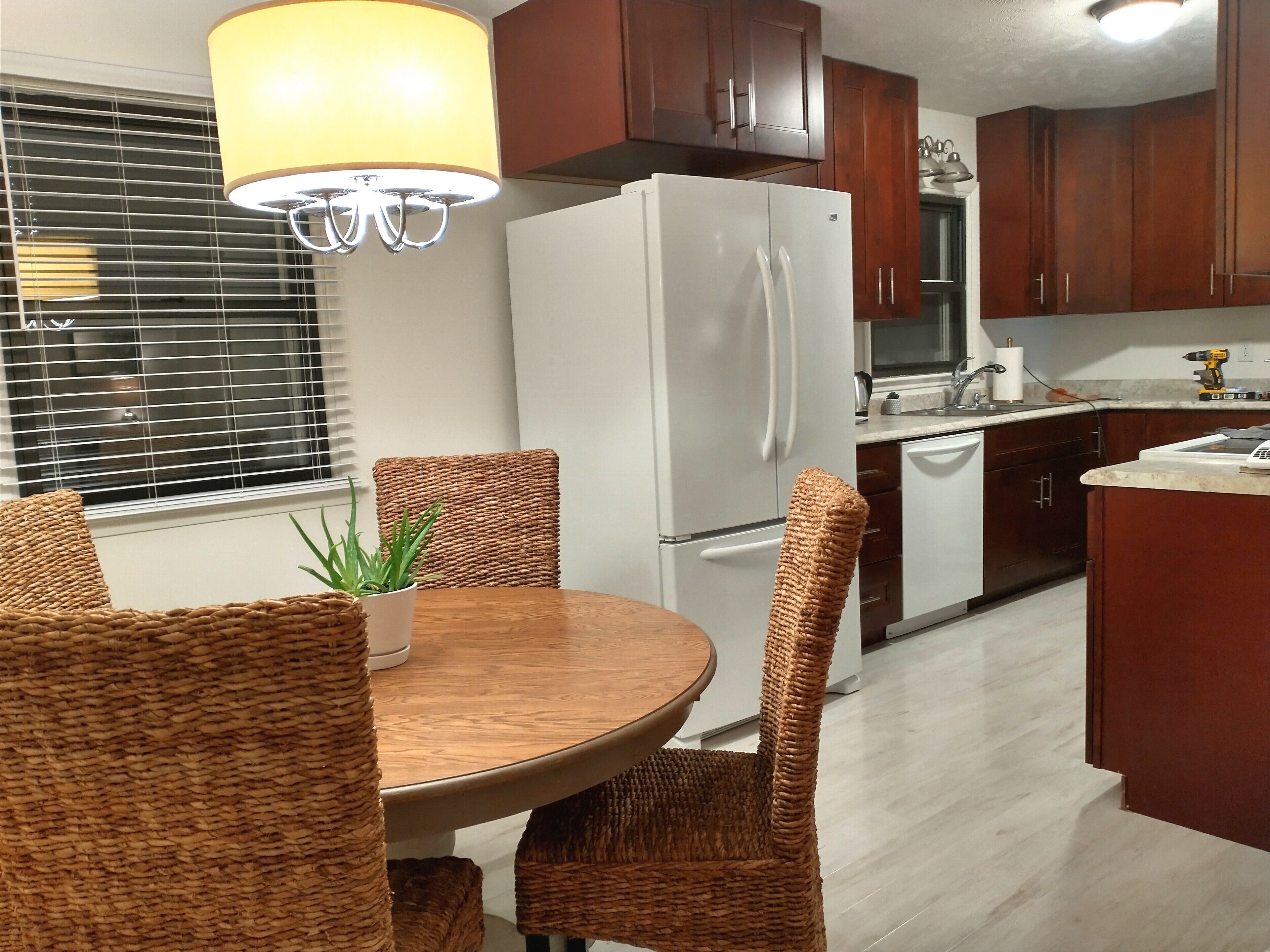 A modern kitchen with a white refrigerator, wooden cabinets, and a dining area with wicker chairs and a round table.