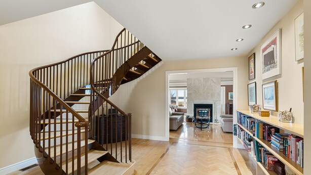 A spacious living area with a wooden herringbone floor, a modern spiral staircase, and a bookshelf filled with books. - Spacious 4 bedrooms Villa, 30 min from Moncton (Cocagne)