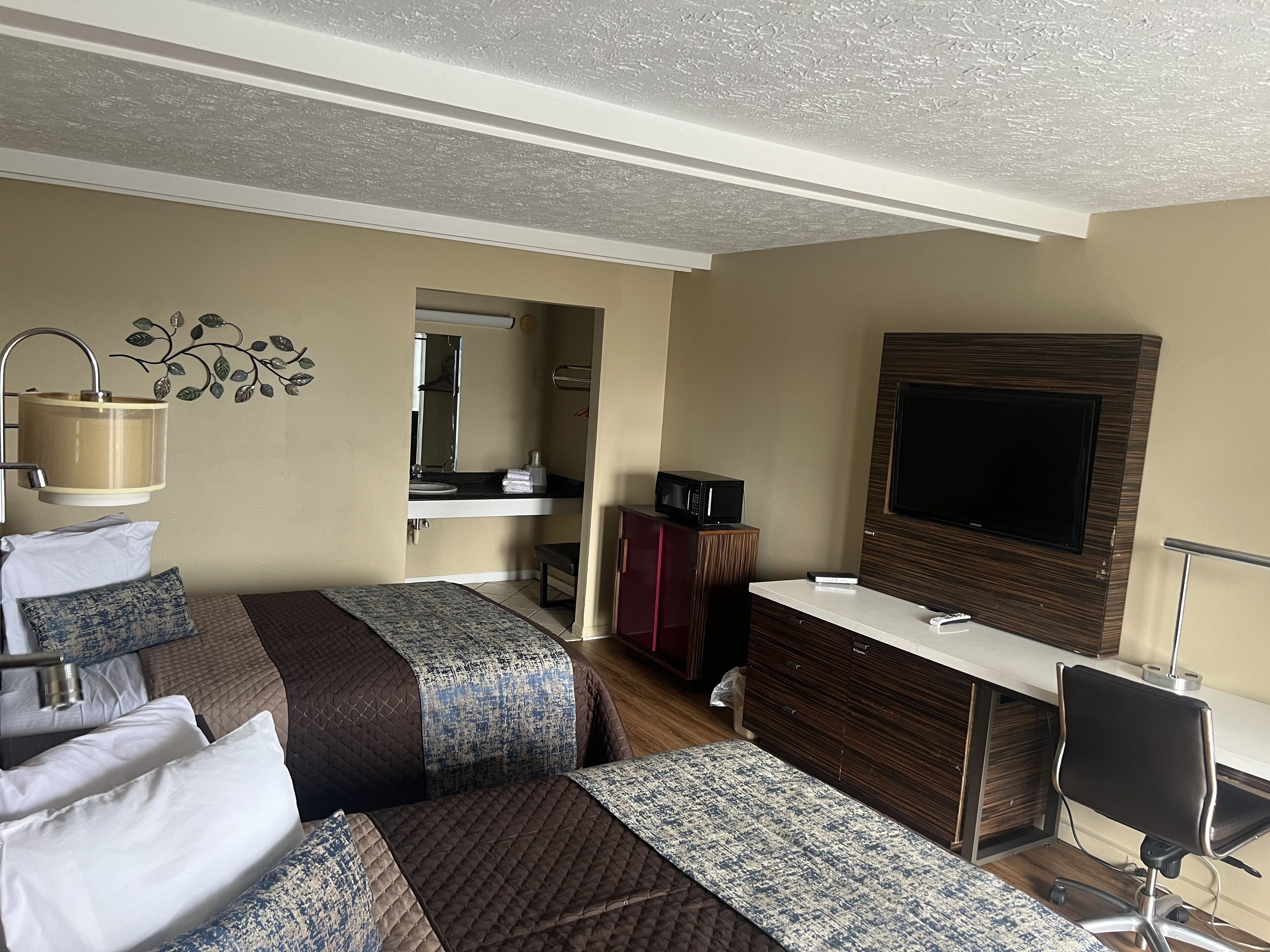 A hotel room with two beds, a desk, a TV, and a bathroom visible through an open door.