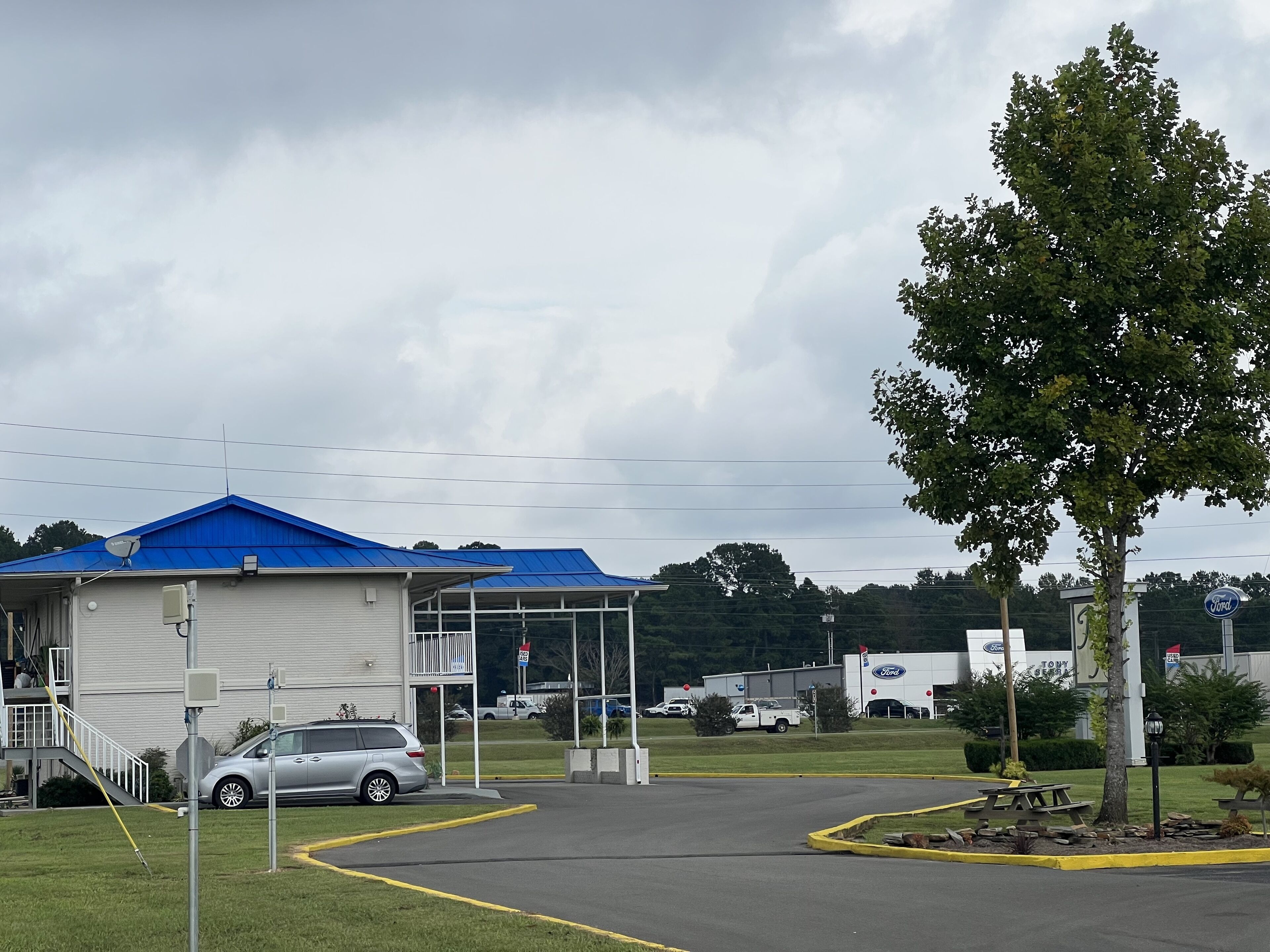 Un edificio comercial con techo azul, estacionamiento y zona de picnic.