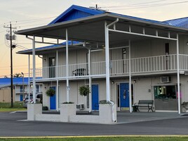 Um motel com estrutura em dois andares, varanda coberta na frente e uma porta azul.