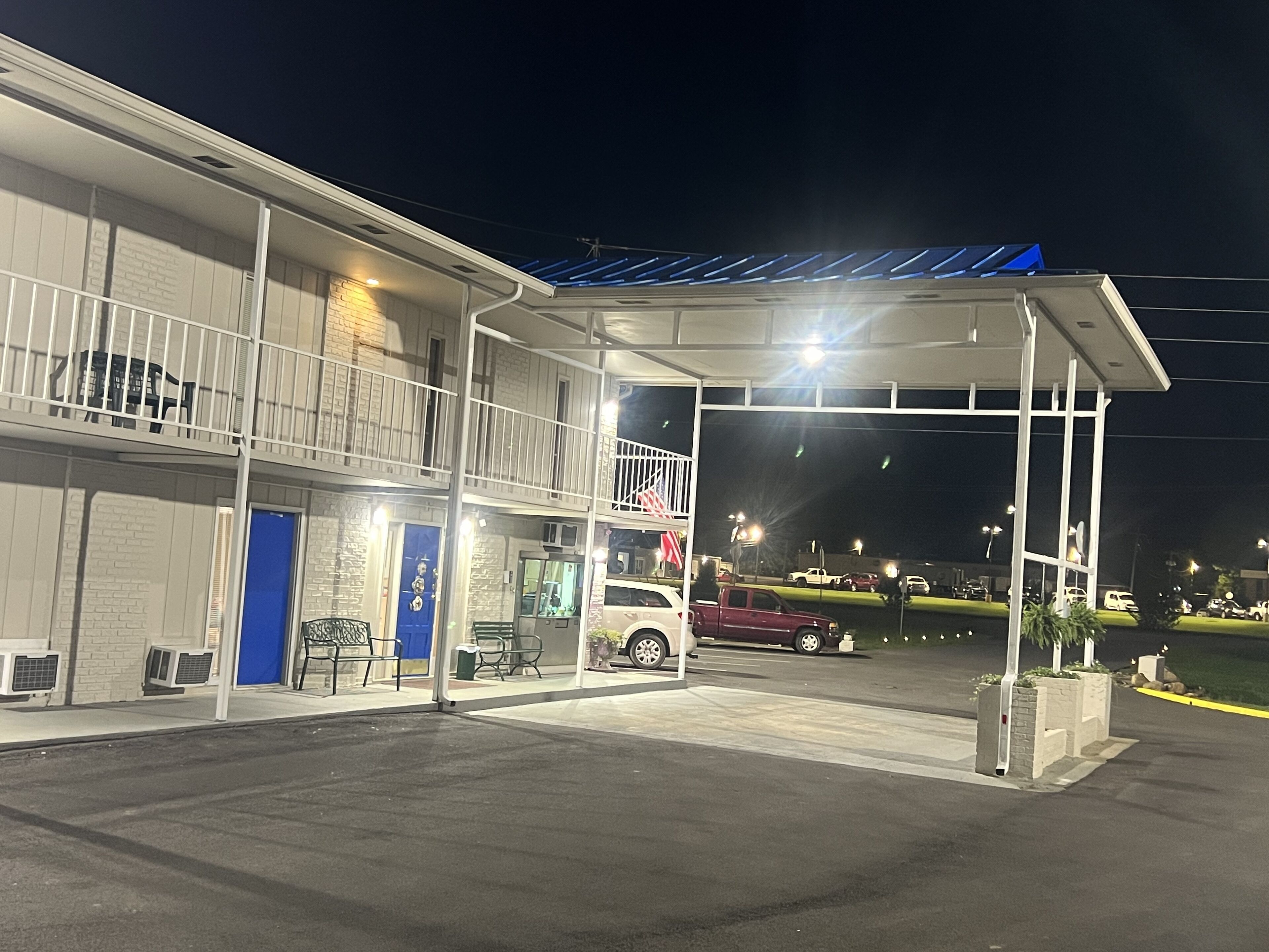Motel amb àrea de pàrquing coberta, una porta blava i una bandera a l'exterior.