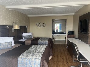 A hotel room with two beds, a desk, a chair, a TV, a mirror, and a bathroom visible through an open door.