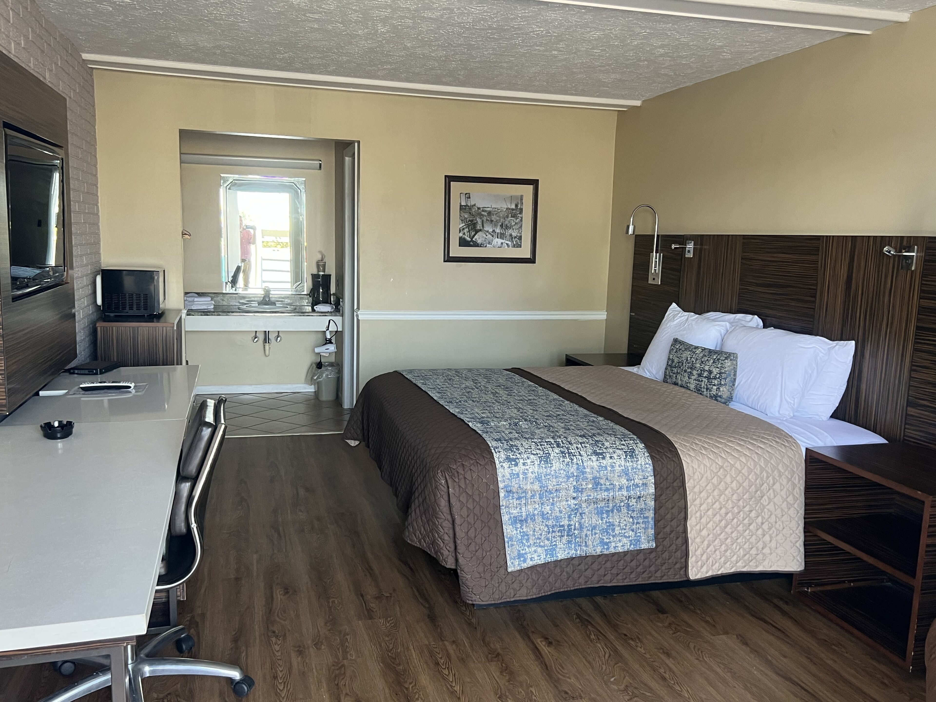 A hotel room with a bed, a desk, a chair, a television, a mirror, and a picture on the wall.