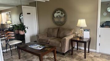 A living room with a brown sofa, a coffee table with magazines, a lamp, and a decorative wall piece.