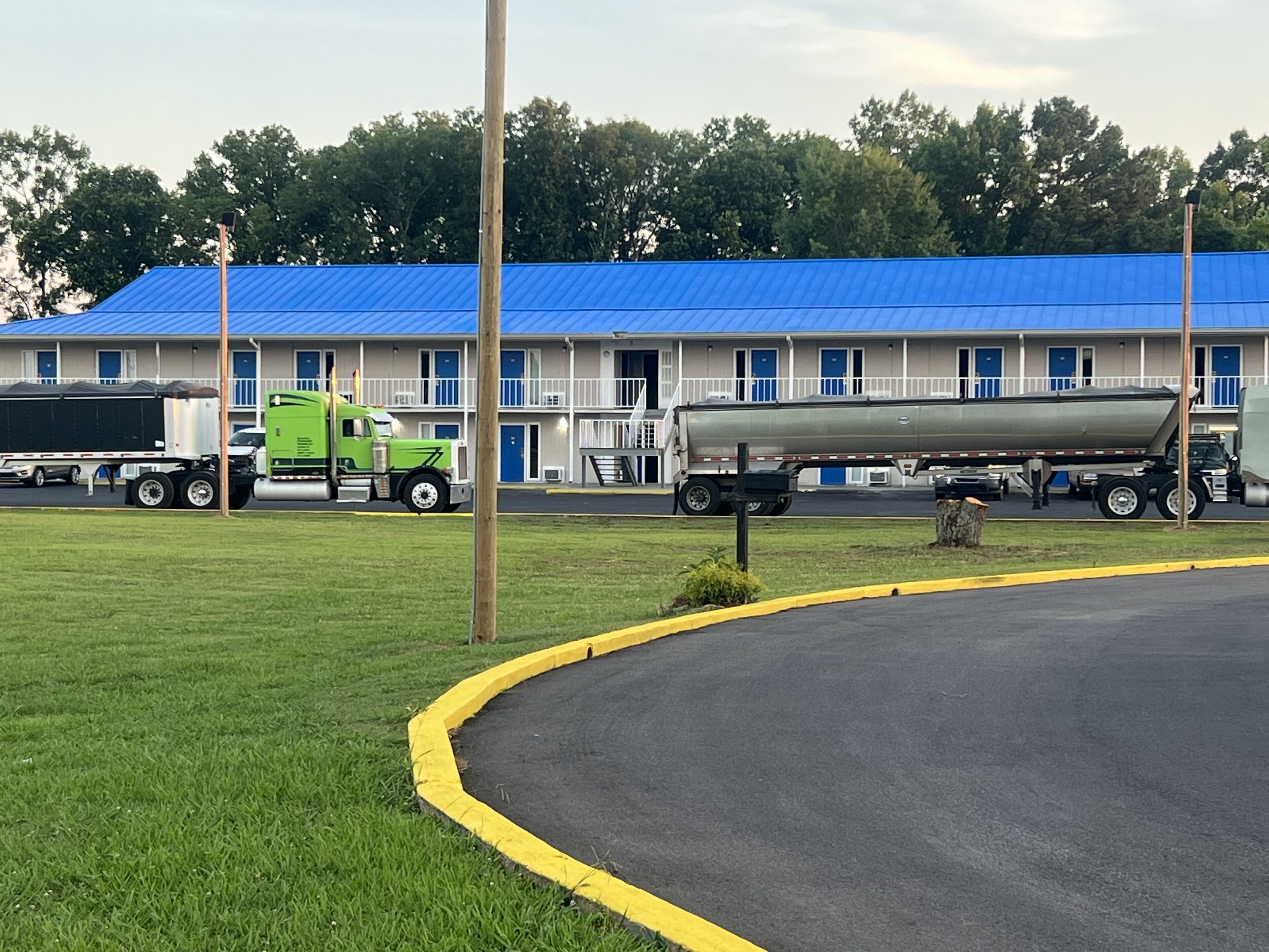 A motel with a blue roof, a parking lot, and several trucks parked in front.