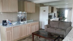A compact kitchen with a coffee machine, a refrigerator, and a sofa in a living area. - Towne Inn (Sylacauga)