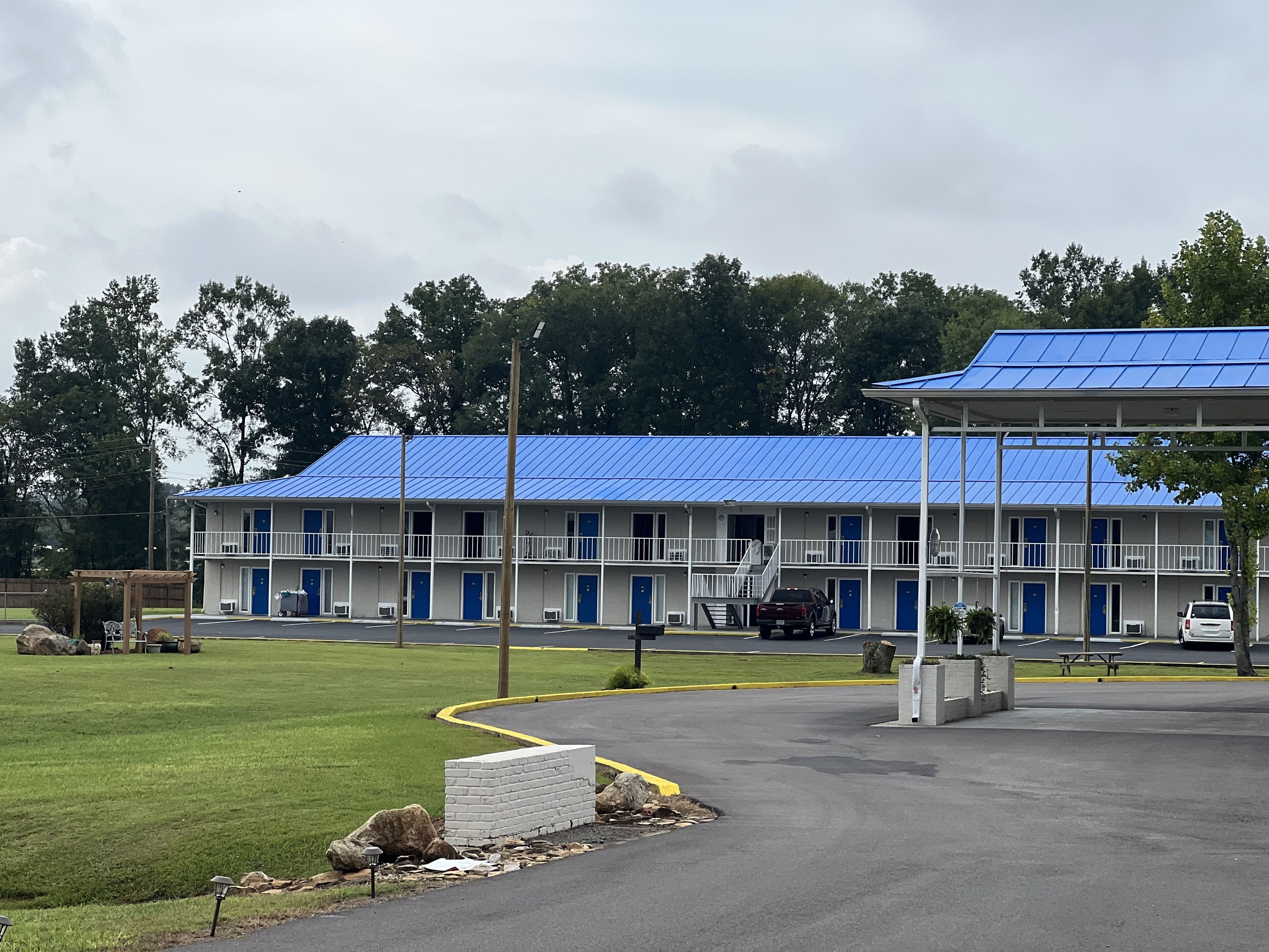 Un motel con techo azul, varias habitaciones y un estacionamiento.
