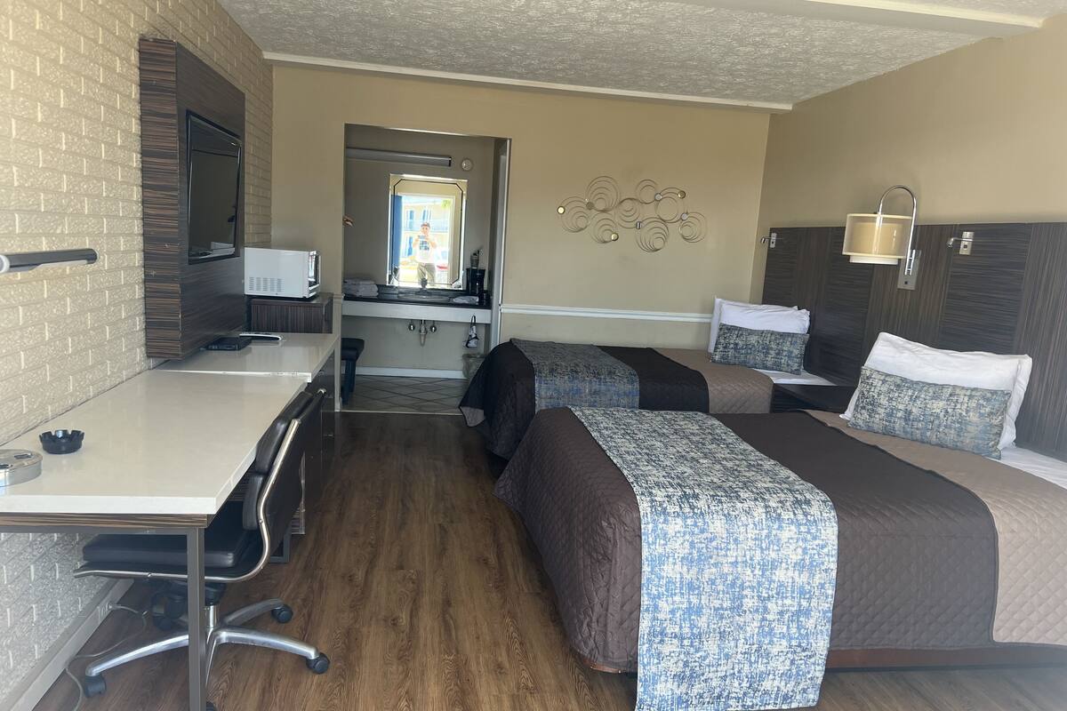 Quarto de hotel com escrivaninha, duas camas, banheiro e vista para a rua.