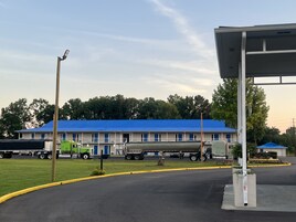Un motel con techo azul, zona de estacionamiento techada y una camioneta estacionada al frente.
