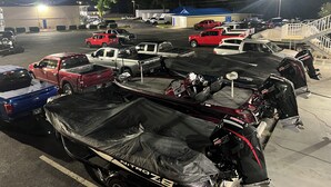 A parking lot with several vehicles, including trucks and a boat covered with a tarp. - Towne Inn (Sylacauga)