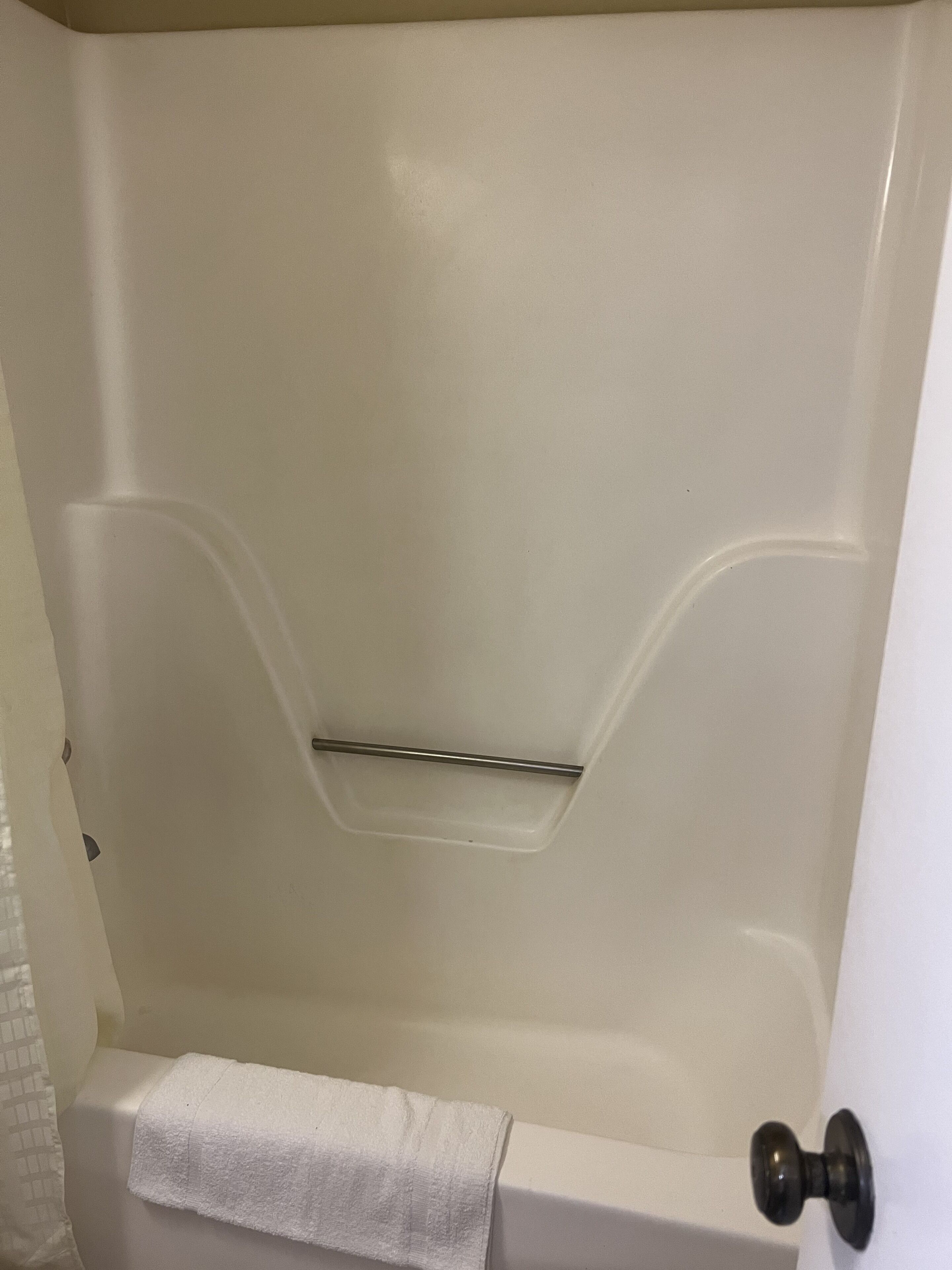 A white bathtub with a towel on the side, a metal grab bar, and a black door knob.