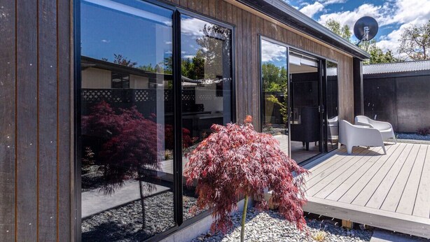 A modern house with large glass doors, a wooden deck, and outdoor furniture. - The Green Room Maryburn Magic (Twizel)