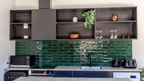 A modern kitchen with a green tiled backsplash, a built-in microwave, a coffee maker, and a dishwasher. - The Green Room Maryburn Magic (Twizel)
