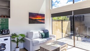 A modern living room with a sofa, coffee table, and a large window overlooking a garden. - The Green Room Maryburn Magic (Twizel)
