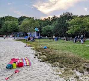 Uma praia com parquinho, mesas para piquenique e uma área de areia com equipamentos de praia.