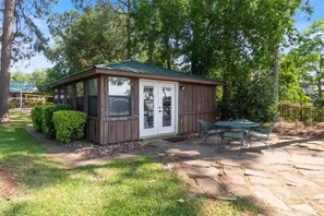 A small wooden cabin with a green roof, a patio with a table and chairs, and a well-maintained lawn. - Waterfront, 2 mins to town, amazing patio, fire pit & more (Gun Barrel City)