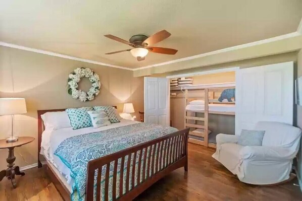 A bedroom with a bed, bedside lamps, a ceiling fan, a wardrobe, and a covered chair.