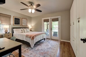 A bedroom with a bed, a ceiling fan, a desk, and a window with blinds.
