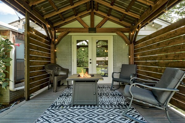 A covered patio with a fire pit, two chairs, and a patterned rug.
