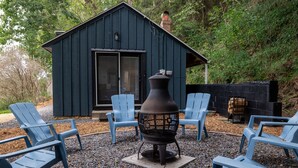 Una cabaña rústica con chimenea, un hoyo de fuego y sillas Adirondack azules.