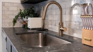 Una cocina con un lavamanos de acero inoxidable, armarios oscuros y un salpicadero de mármol.