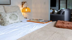 Un dormitorio moderno con cama, lámpara de noche y vista a otra habitación.