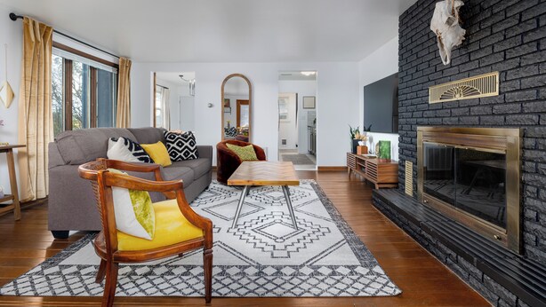 Una sala de estar con chimenea, un sofá, una mesa de centro de madera y un tapete estampado.