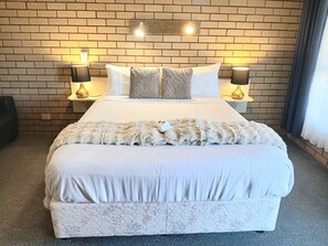 Una habitación de hotel con una pared de ladrillo, una cama grande con ropa blanca, dos lámparas de noche y una manta suave.