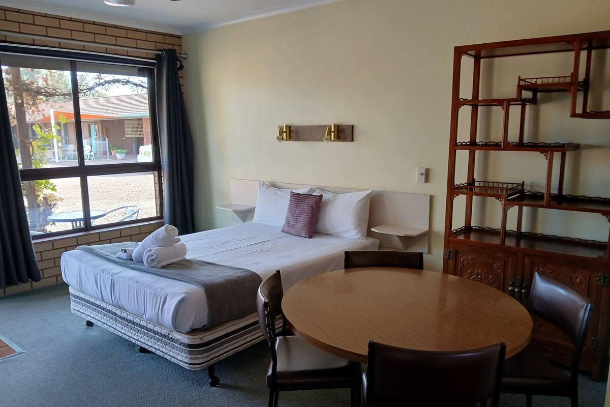 Una habitación de hotel con una cama, una mesa redonda de madera y una silla.