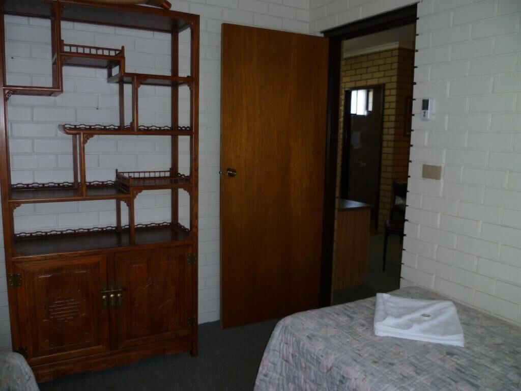 Quarto com cama, um armário de madeira e porta que dá para outro cômodo.