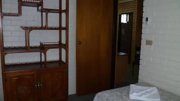 Quarto com cama, um armário de madeira e porta que dá para outro cômodo.