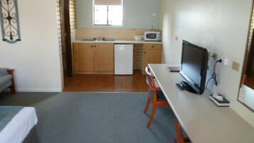 A compact room with a bed, a desk with a computer, a microwave, and a small kitchenette with a sink and a refrigerator.