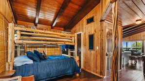 Een rustiek houten chalet van binnen, met een stapelbed, houten wanden en een eethoek zichtbaar door een open deur.